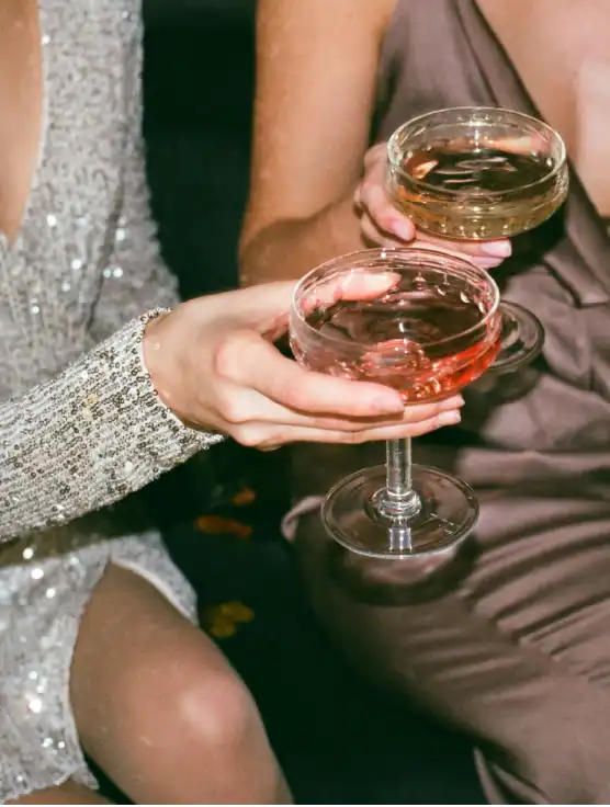 Two elegantly dressed women toasting with sparkling wine and rosé cocktails at a glamorous event in Mallorca.