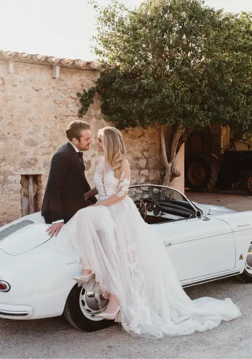 Bride and groom sharing a romantic moment after their destination wedding in Mallorca, posing with a classic white vintage car in finca Biniorella.