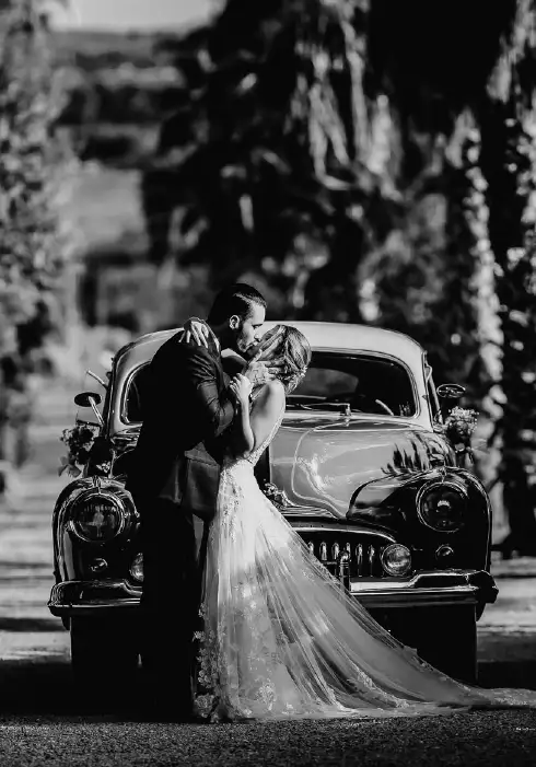 Bride and groom are kissing in front of a vintage car at their wedding in Mallorca