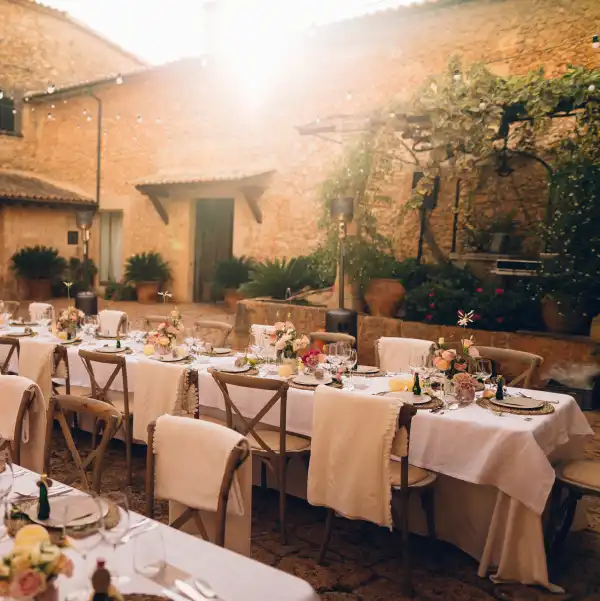 A beautifully set outdoor luxury dinner event in Mallorca, featuring rustic stone walls, floral centerpieces, and warm lighting