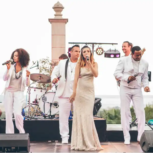 A live band performing at an event in Mallorca, featuring vocalists and musicians dressed in elegant white attire on an outdoor stage.
