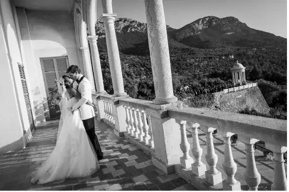 A newlywed couple embracing on a balcony at Son Marroig during their elopement in Mallorca, with breathtaking scenery in the background.