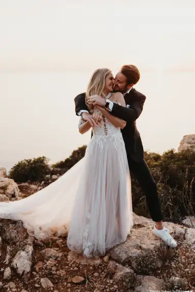 A joyful couple embracing on a rocky cliff after their destination wedding in Mallorca, with the Mediterranean Sea and a golden sunset in the background